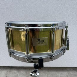 Zlatý buben s chromovanými obručemi a mechanismy, umístěný na chromovaném stojanu. Na korpusu je čtvercový štitek s nápisy Pearl, MADE IN TAIWAN a Br…