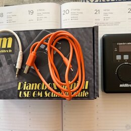 Černý kompaktní modul s nápisy Pianobox mini II, USB, MIDI a miditech. K zařízení patří oranžový kabel a bílý kabel s konektorem a logem miditech. Vš…