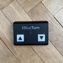 Černý obdélníkový ovladač s nápisem iRig BlueTurn. Zařízení má dvě bílá čtvercová tlačítka s černými šipkami směřujícími nahoru a dolů, nad nimi jsou…