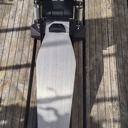 Na dřevěném podkladu leží elektronický pedál basového bubnu v černé a stříbrné barvě. Na spodní části stříbrného šlapadla je umístěn nápis Roland. V…