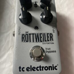 Stříbrný efekt pedál s nápisy RÖTTWEILER DISTORTION, true bypass a tc electronic®. Na horní části jsou čtyři černé oválné ovládací knoflíky a nápisy…
