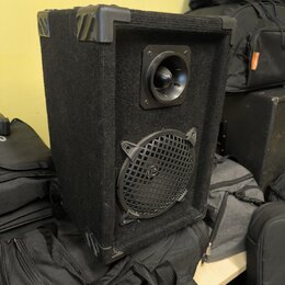 Černý aktivní reproduktor v bedně potažené textilií s plastovými rohy. V horní části je umístěn vysokofrekvenční měnič a v dolní části větší reproduk…