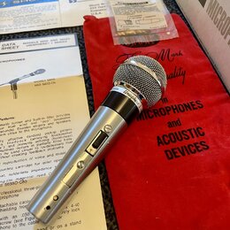 Stříbrný dynamický mikrofon s mřížkou a šedým tělem, na kterém je nápis Unisphere I. Mikrofon leží na červeném textilním pouzdře s nápisem Shure Mark…