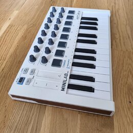 Bílá MIDI klaviatura s 25 klávesami a ovládacími prvky v horní části. Na přístroji je uveden nápis MINILAB mkII a značka ARTURIA. Obsahuje několik še…