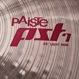 Detailní záběr na povrch mosazného činele s viditelným rýhováním. Na povrchu je červený nápis PAiste a pod ním stylizovaný červený nápis pst7 s doplň…