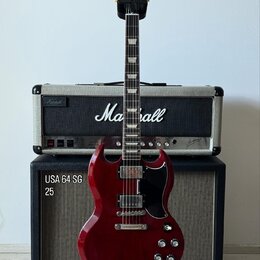 Elektrická kytara v tmavě červené barvě s černým pickguardem, umístěná na stojanu. Na hlavě hmatníku je nápis Gibson a na kombu v pozadí značka Marsh…