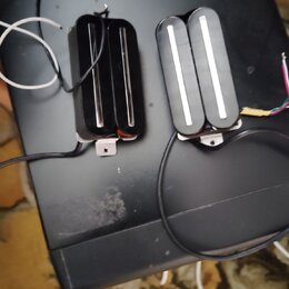 Dvě černé humbucker snímače s bílými plastovými krytkami nad pólky. Snímače jsou vybaveny připojovacími kabely a kovovými montážnímideskami. Na povrc…
