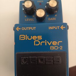 Modrý efekt pedál s nápisy Blues Driver a BD-2. Na spodním černém spínači je vyražené logo BOSS. Horní část obsahuje tři ovládací knoflíky s popisky…