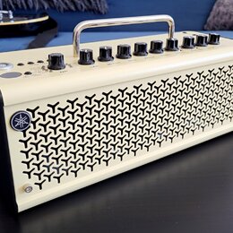 Kytarový kombozesilovač krémové barvy s kovovou rukojetí nahoře. Na předním panelu jsou ovládací knoflíky a nápisy GAIN, MASTER, REVERB. Přední mřížk…
