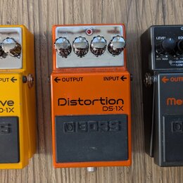 Tři kytarové efekty značky BOSS v žluté, oranžové a černé barvě. Horní pedál má nápisy OverDrive OP-1X, prostřední Distortion DS-1X a spodní Metal Zo…