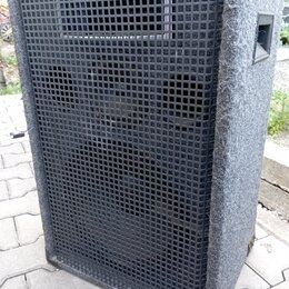Šedý reproduktorový box s povrchem z textilu a černou plastovou mřížkou. V horní části je umístěn menší obdélníkový reproduktor a pod ním dva větší k…