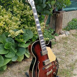 Polodupatá elektrická kytara s tmavě hnědým lakem v přechodu (sunburst) a zlatými prvky. Na hlavě je bílý nápis Epiphone. Nástroj má dva humbuckery,…