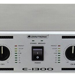 Stříbrný rackový zesilovač značky OMNITRONIC s modelem E-1300. Přední panel obsahuje dva ovratidla pro CH 1 a CH 2, vypínač POWER a dvě sady LED indi…