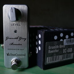 Stříbrný efekt pedál z broušeného kovu s jedním ovládacím knoflíkem a spínacím tlačítkem. Na povrchu jsou nápisy LEVEL, Granith Grey Booster, DESIGNE…