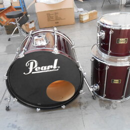 Sada bubnů v tmavě červené barvě. Na černém předním koži basového bubnu je bílý nápis Pearl®. Tom a floor tom mají na korpusu zlaté štítky s nápisem…