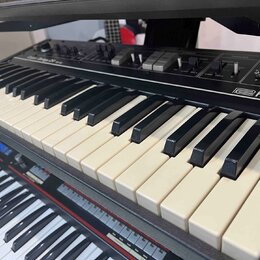 Detailní pohled na klávesnice dvou elektronických klavírů umístěných nad sebou. Horní nástroj je černé barvy s nápisem Roland a viditelnými ovládacím…