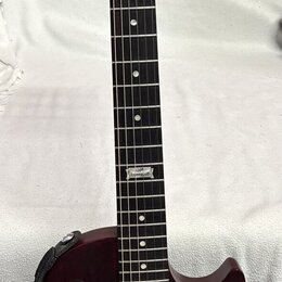 Tmavě červená elektrická kytara typu Les Paul s černým hmatníkem a dvěma humbuckery. Na hlavě je bílý nápis Gibson a pod ním kurzívou Les Paul Model.…