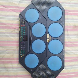Elektronický bicí pad modré barvy s černým plastovým rámem. Na přístroji je nápis YAMAHA a model DD-12, dále text Super Session Pad / Player / Scrape…