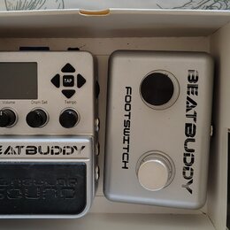 V bílém kartónovém boxu jsou dvě stříbrná zařízení. Levý pedál má nápisy BEATBUDDY a Singular Sound, horní ovládací panel s displejem a popisky Volum…