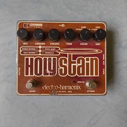 Efektový pedál v hnědo-oranžové barvě s nápisem Holy Stain. Na horní části jsou šest černých otočných ovladačů s popisky MIX, AMOUNT, VOLUME, TONE, C…