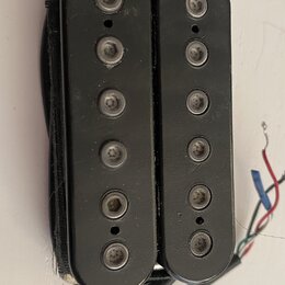 Dva černí elektrické snímače typu humbucker s viditelnými polosnovými póly. Povrch je černý, matný a vykazuje drobné škrábance a prach. Z pravého sní…