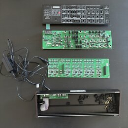 Na černém stole leží rozložený elektronický hudební přístroj. Horní část tvoří ovládací panel s nápisem Pro-1700, řadou tlačítek a zahlreichen potenc…