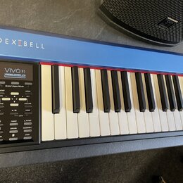 Digitální piano v modré barvě s bílými a černými klávesami. Na horní liště je bílý nápis DEXIBELL a v ovládacím panelu nápisy VIVO S1, Grand Piano Mo…