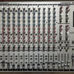 Stříbrný míchací pult s nápisy BEHRINGER® ULTRA-LOW NOISE DESIGN a EURORACK MX 2642A 26 INPUT 4-BUS MIXING CONSOLE. Zařízení obsahuje řady šedých, mo…