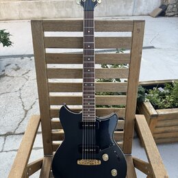 Černá elektrická kytara s tmavým hmatníkem a zlatými prvky. Na hlavě je viditelné logo Yamaha, na korpusu jsou dva humbuckery a tři ovládací knoflíky…