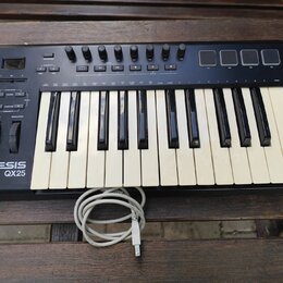 Černý kompaktní MIDI kontrolér s klávesnicí, umístěný na dřevěném stole. Na levé straně je bílý nápis ALESIS QX25 a ovládací prvky v podobě tlačítek,…