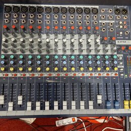 Modrý mixovací pult s kovovým šasi a řadou vertikálních posuvníků. V pravém horním rohu je nápis Soundcraft a dále modelové označení EPM12. Zařízení…