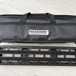 Černý textilní softcase s rukojetmi a modrým detailem u zipu. Na přední straně je bílý štítek s nápisem ROCKBOARD® by WARWICK. Pod pouzdrem leží čern…