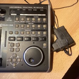 Šedý kontrolní povrch s nápisem UNIVERSAL CONTROL SURFACE a logem behringer. Na levé straně je vidět označení X-TOUCH ONE, jeden posuvník a ovládací…
