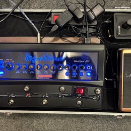 V otevřeném hliníkovém kufru se nachází černý kytarový zesilovač s modře podsvíceným panelem, na kterém je nápis Hughes & Kettner a model Black Spiri…
