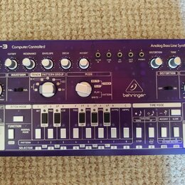 Bílo-fialový analogový syntetizátor s nápisy TD-3 Computer Controlled a Analog Bass Line Synthesizer. Na přístroji je viditelné logo behringer a řada…