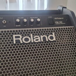 Černý osobní monitor s kovovou mřížkou, na které je bílý nápis Roland. Horní ovládací panel obsahuje vstupy INPUT (V-Drums, LINE), ovladače VOLUME (V…
