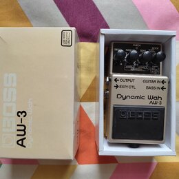 Krabice a efekt pedál značky BOSS model AW-3 Dynamic Wah. Pedál je umístěn v bílé krabičce a má stříbrné tělo s černým spínacím pedálem, na kterém je…