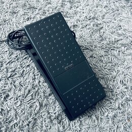 Černý sustain pedál z plastu s texturovaným povrchem v podobě vyvýšených teček. Uprostřed je viditelný nápis YAMAHA. K pedálu vede černý kabel s kone…