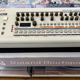 Bílá rytmická sekvenční jednotka s nápisy Roland a TR-09 v horní levé části a RHYTHM COMPOSER v pravé. Zařízení obsahuje řadu černých otočných ovlada…