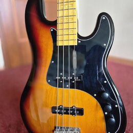 Elektrická basová kytara s korpusem v barevném přechodu od žluté přes oranžovou k červené a černé. Nástroj má černý pickguard, čtyři ovládací knofíky…