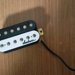 Černý humbucker s bílým plastovým krytem. Na krytu je černý nápis jackson. Snímač má připojení v podobě černého kabelu a vykazuje mírné znečištění po…