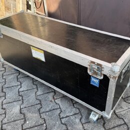 Černý transportní flightcase s hliníkovými hranami a kovovými rohy. Na boku je umístěna žlutá varovná nálepka a modrý štítek s nápisem THON. Povrch v…