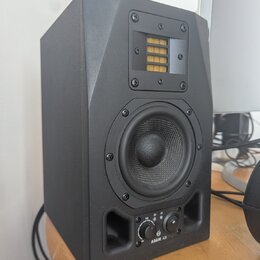 Černý studiový monitor v hranaté skříni. V horní části je umístěn páskový výšek s žlutým membránovým prvkem, uprostřed je kruhový střední reproduktor…
