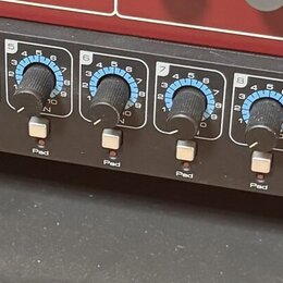 Detailní pohled na přední panel černého rackového audio zařízení. Panel obsahuje řadu modrých otočných ovladačů, bílá tlačítka s nápisy „Inst“ a „Pad…