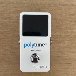 Bílý kytarový tuner s černým displejem. Na přední straně je modrý a šedý nápis polytune3, pod ním text TRUE | BUFFER a ve spodní části logo s nápisem…