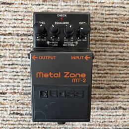 Černý efekt pedál s oranžovými nápisy Metal Zone a MT-2. Na horní části jsou čtyři ovládací knoflíky s popisky VEL, EQUALIZER (HIGH, LOW, MIDDLE, MID…