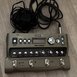 Šedý looper značky LINE 6 s nápisem JM4 Looper. Zařízení má několik ovládacích knoflíků, tlačítka a displej, nad kterým jsou nápisy GUITAR, MIC/AUX,…