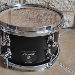 Černý buben s chromovaným obručováním a mechanismy. Na korpusu je nalepený štítek s nápisy SONOR, Sonic Rain a MADE IN GERMANY. Na horním blaně je vi…