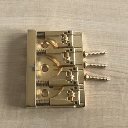 Zlatý kovový kobylkový mechanismus s třemi saddlesy a třemi přiloženými šrouby. Povrch je lesklý, bez viditelných značek, log nebo nápisů. Předmět vy…