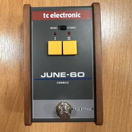 Šedý efekt pedál s dřevěným rámem a červeným horním panelem. Na zařízení jsou nápisy tc electronic, MONO, STEREO, I, II, JUNE-60, CHORUS a TRUE BYPAS…